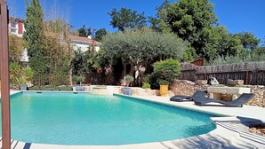 A swimming pool with lounge chairs and a stone wall in the background.