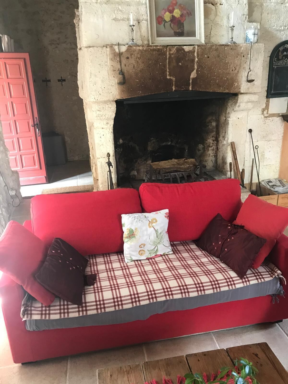 Un canapé rouge agrémenté de coussins à carreaux et à motifs floraux, une cheminée et une porte rouge.