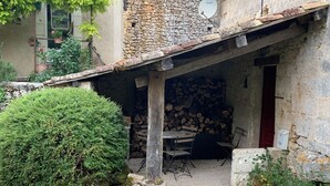 Ein rustikales Steinhaus mit überdachter Terrasse, einem kleinen Tisch und Stühlen sowie einem ordentlich gestapelten Holzstoß.