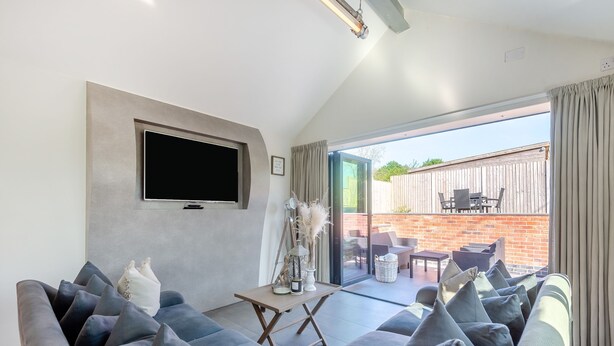 A living room with a large grey sofa, a flat-screen TV mounted on the wall, and a sliding glass door leading to an outdoor patio with outdoor furniture. - 1 bedroom accommodation in Meriden, near Coventry (Meriden, near Coventry)