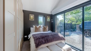 A modern bedroom with a large bed, a glass door leading outside, and a view of a vehicle.
