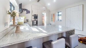 A modern kitchen with a marble countertop, built-in oven, and seating area with cushioned chairs.