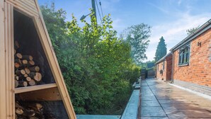 A wooden structure with stacked firewood, a bench, and a brick building in the background. - 1 bedroom accommodation in Meriden, near Coventry (Meriden, near Coventry)