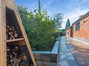A wooden structure with stacked firewood, a bench, and a brick building in the background. - 1 bedroom accommodation in Meriden, near Coventry (Meriden, near Coventry)