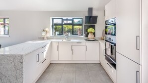 A modern kitchen with white cabinets, a marble countertop, a black range hood, and a large window with a view of greenery. - 1 bedroom accommodation in Meriden, near Coventry (Meriden, near Coventry)