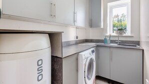 A modern kitchen with a washing machine, grey cabinets, a window with a view, and a sink with a faucet.