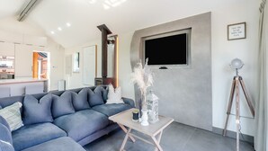 A modern living room with a sectional sofa, a small table with decorative items, a mounted TV, and a tripod lamp. - 1 bedroom accommodation in Meriden, near Coventry (Meriden, near Coventry)