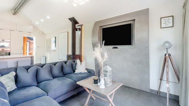 A modern living room with a sectional sofa, a small table with decorative items, a mounted TV, and a tripod lamp.