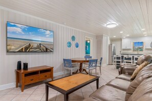 A living room with a wooden coffee table, a sofa, and a TV mounted on the wall. - 5 BR Dog Friendly Home- Slps 12- Steps from sand (North Myrtle Beach)