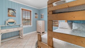 Une chambre avec un lit superposé, une commode, une coiffeuse avec un miroir et deux fenêtres équipées de stores.