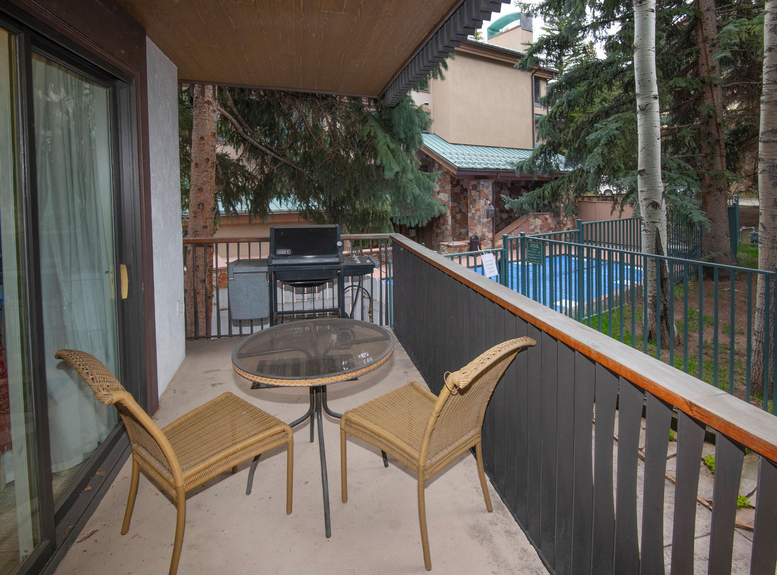 A balcony with wicker chairs, a glass table, and a grill.