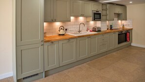 A kitchen with light green cabinets, a wooden countertop, a microwave, a toaster, and a sink. - Barn in Cotswolds With Hot Tub & Scenic Views (Cheltenham)