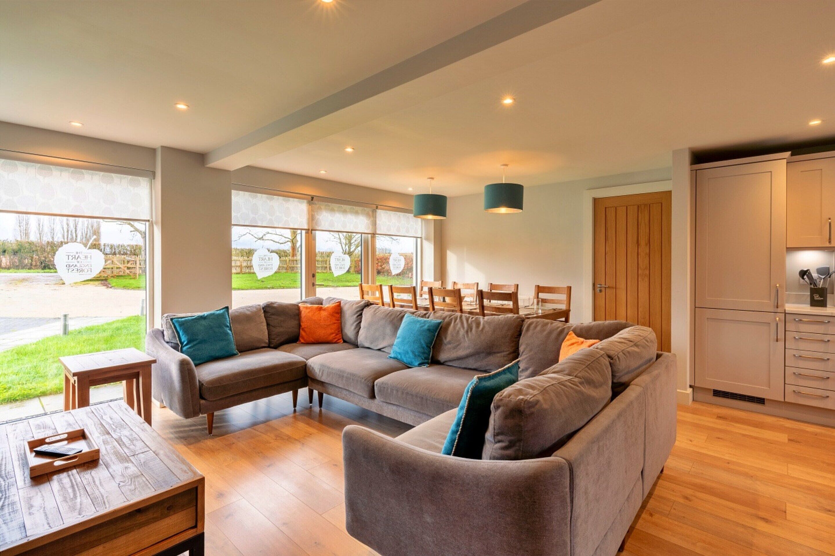 A modern living room with a sectional sofa, wooden coffee table, and a view of the outdoors through large windows.