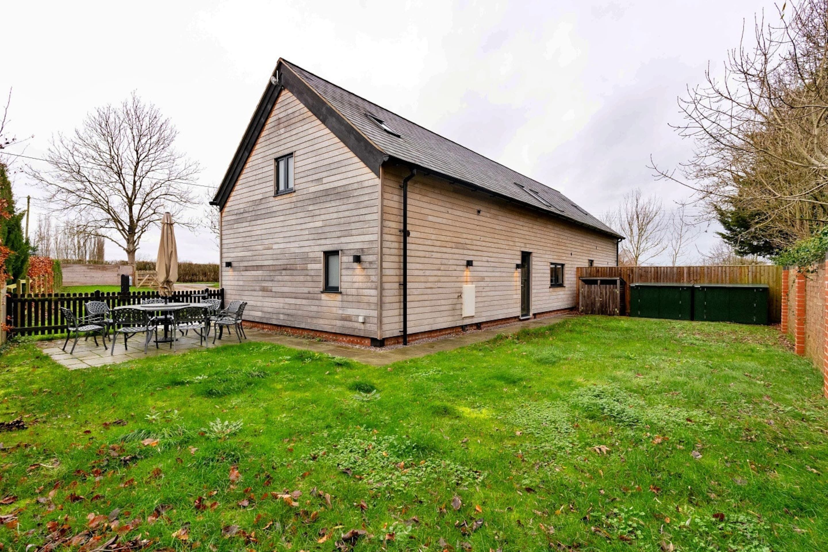 A single-story building with a sloped roof, a fenced backyard, and a patio area with outdoor furniture.