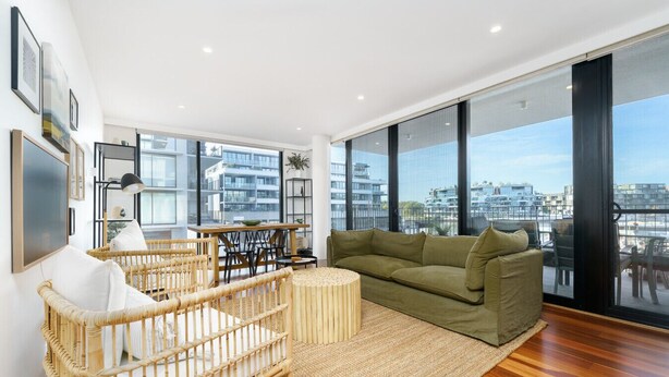A modern living room with a large window, a green sofa, a wicker chair, and a small table. - Vibrant Stay with Lakeside Charm in Kingston (Kingston)