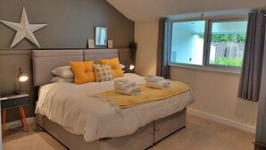 Ein Schlafzimmer mit Bett, Nachttischen, einer Sterndekoration, einem Fenster mit Vorhängen und Blick auf grüne Vegetation außerhalb.