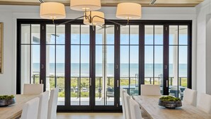 Ein moderner Essbereich mit großem Tisch und Stühlen, großen Fenstern mit Meerblick und einer Decke mit Pendelleuchten.