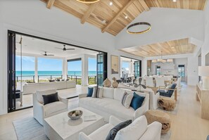 Un vaste espace de vie comprenant un grand canapé blanc, une table basse et une vue sur l’océan.