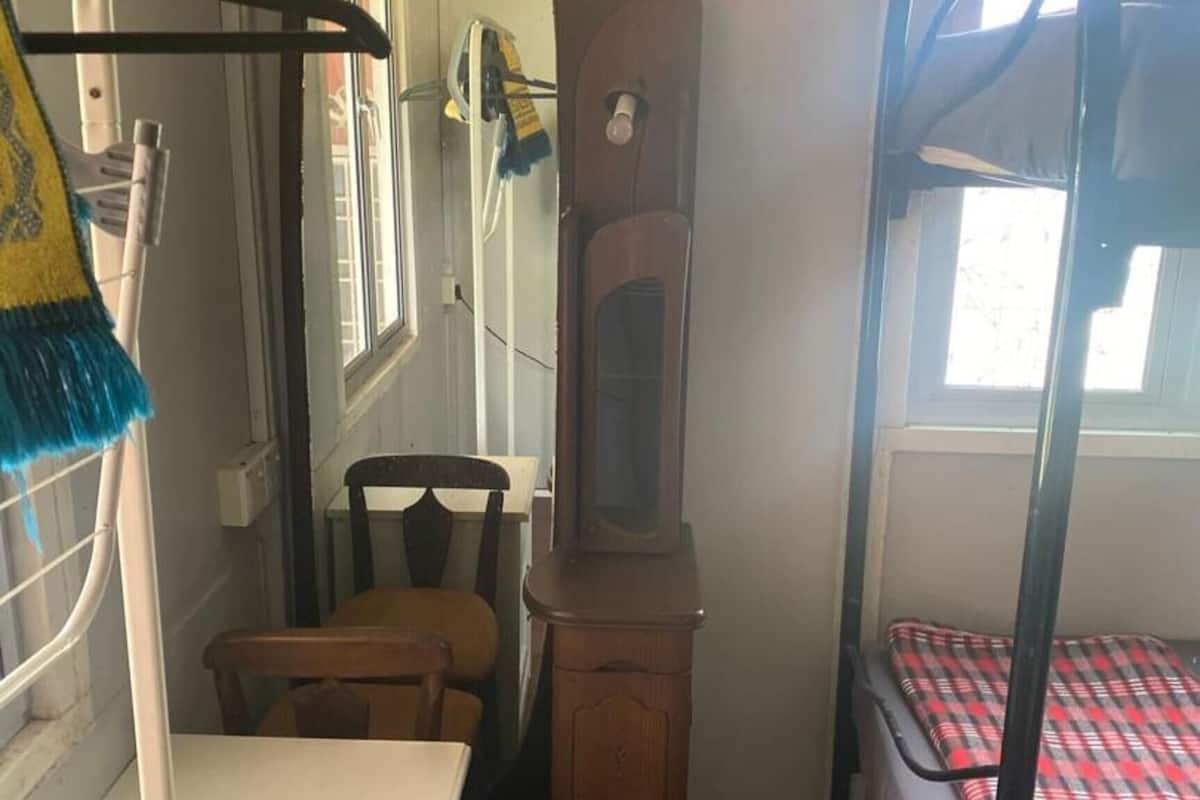 Quarto compacto com beliche, cómoda de madeira, uma cadeira e um espelho.