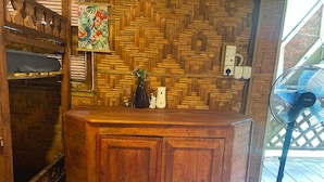 Un comptoir d’accueil en bois, avec un mur décoré d’un motif en chevrons derrière, un ventilateur et une petite plante posée sur le comptoir.