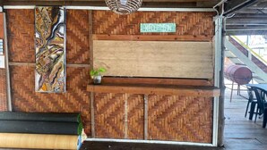 Un espace d’accueil avec un mur orné d’un motif en chevrons, un panneau d’identification pour la réception, un luminaire suspendu et une petite plante posée sur une étagère.