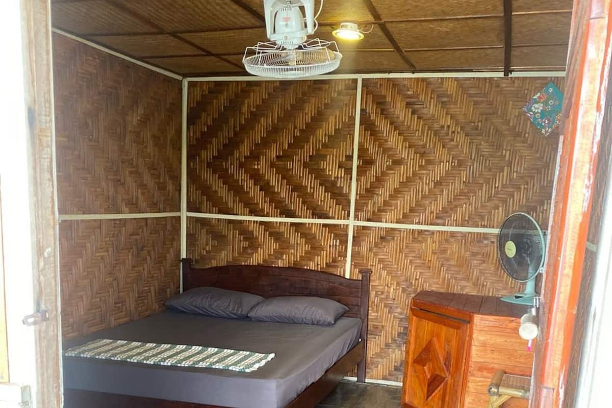 Quarto com cama, escrivaninha pequena, ventilador e ventoinha de teto.