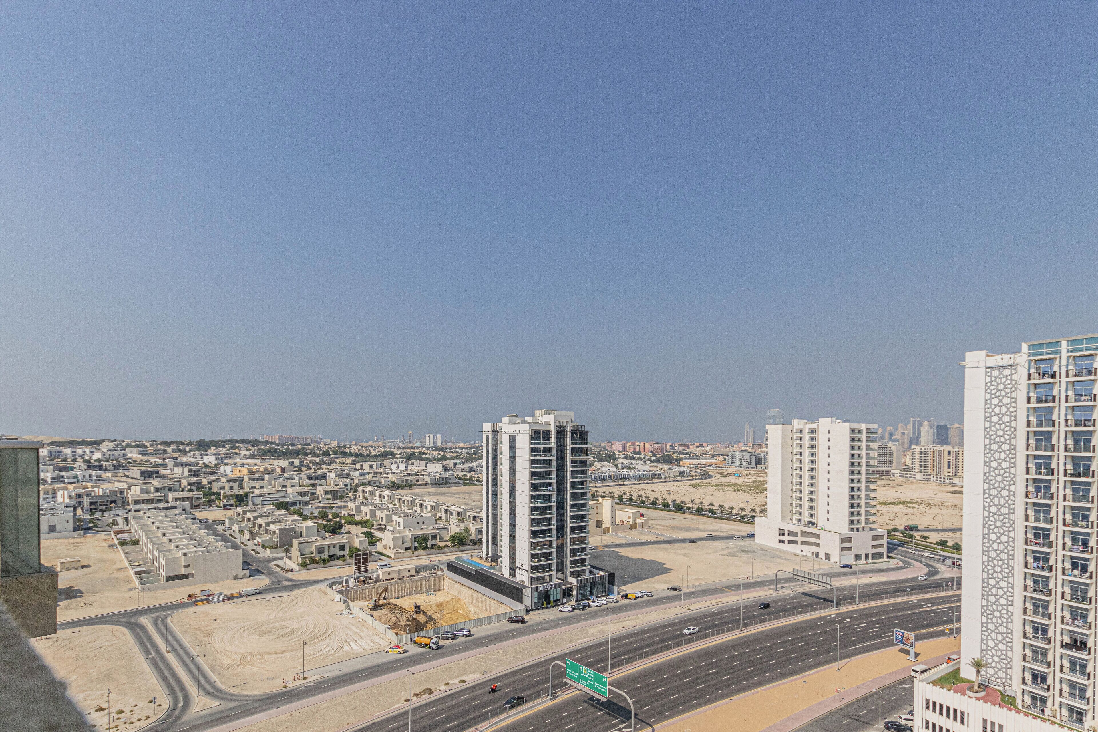 A high-rise building with a modern design, surrounded by a well-developed urban area with wide roads and other buildings.