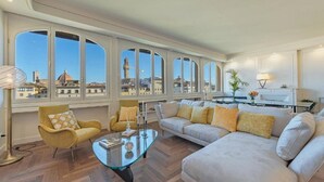 Ein geräumiges Wohnzimmer mit großem Fenster, einer Sofagarnitur, einem Glastisch und einer Lampe.