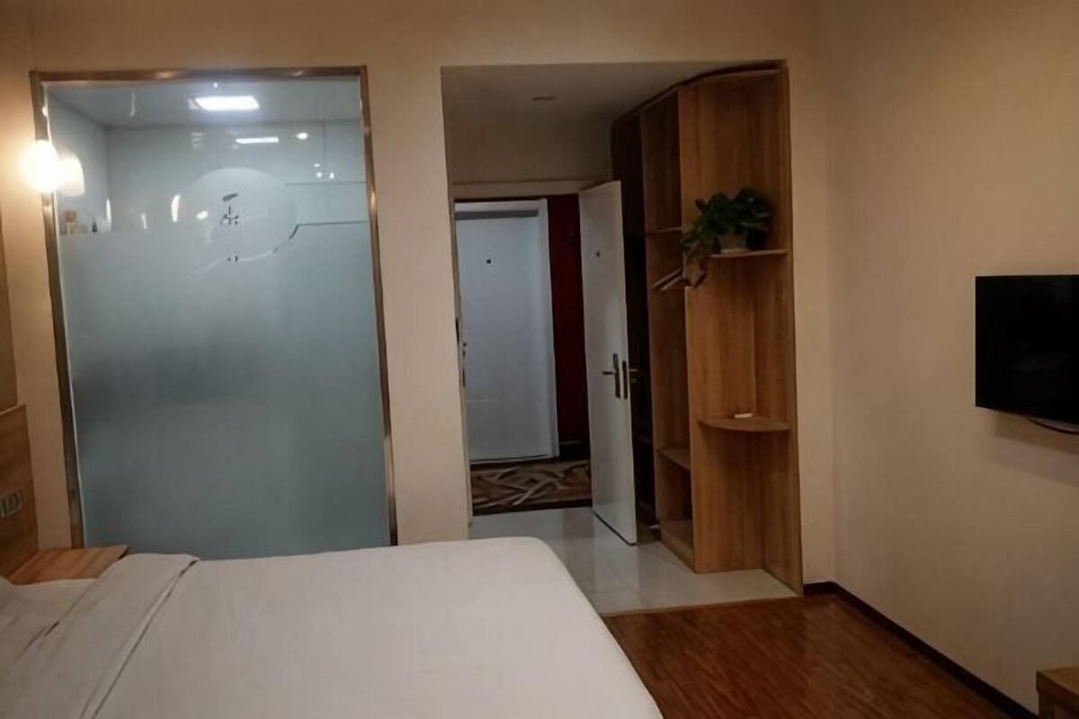 A hotel room with a bed, a wardrobe, a television, and a door leading to another room.