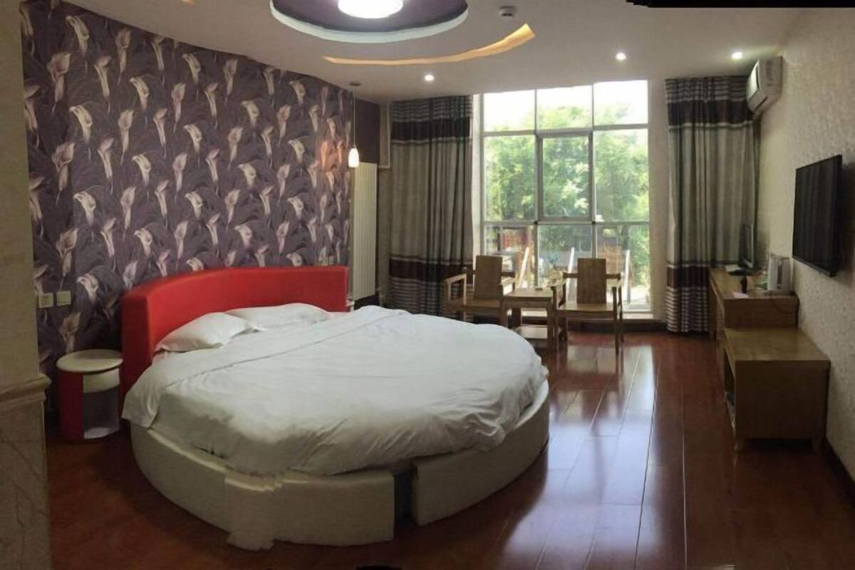 A modern bedroom with a large bed, a small round table, and a TV mounted on the wall.