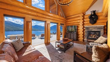 A log cabin interior with a fireplace, leather sofa, and a view of a lake and mountains.