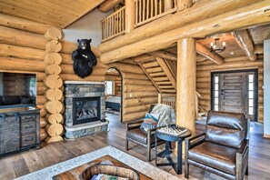 Interior de una cabaña de madera con chimenea de piedra, muebles de cuero y un trofeo de cabeza de oso.