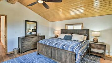 Een slaapkamer met een houten plafond, een bed met een gestreept dekbed, een dressoir, een spiegel en een nachtkastje met een lamp.