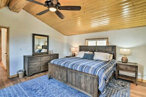 Een slaapkamer met een houten plafond, een bed met een gestreept dekbed, een dressoir, een spiegel en een nachtkastje met een lamp.
