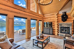 A log cabin interior with a fireplace, a television, and a view of a lake and mountains.