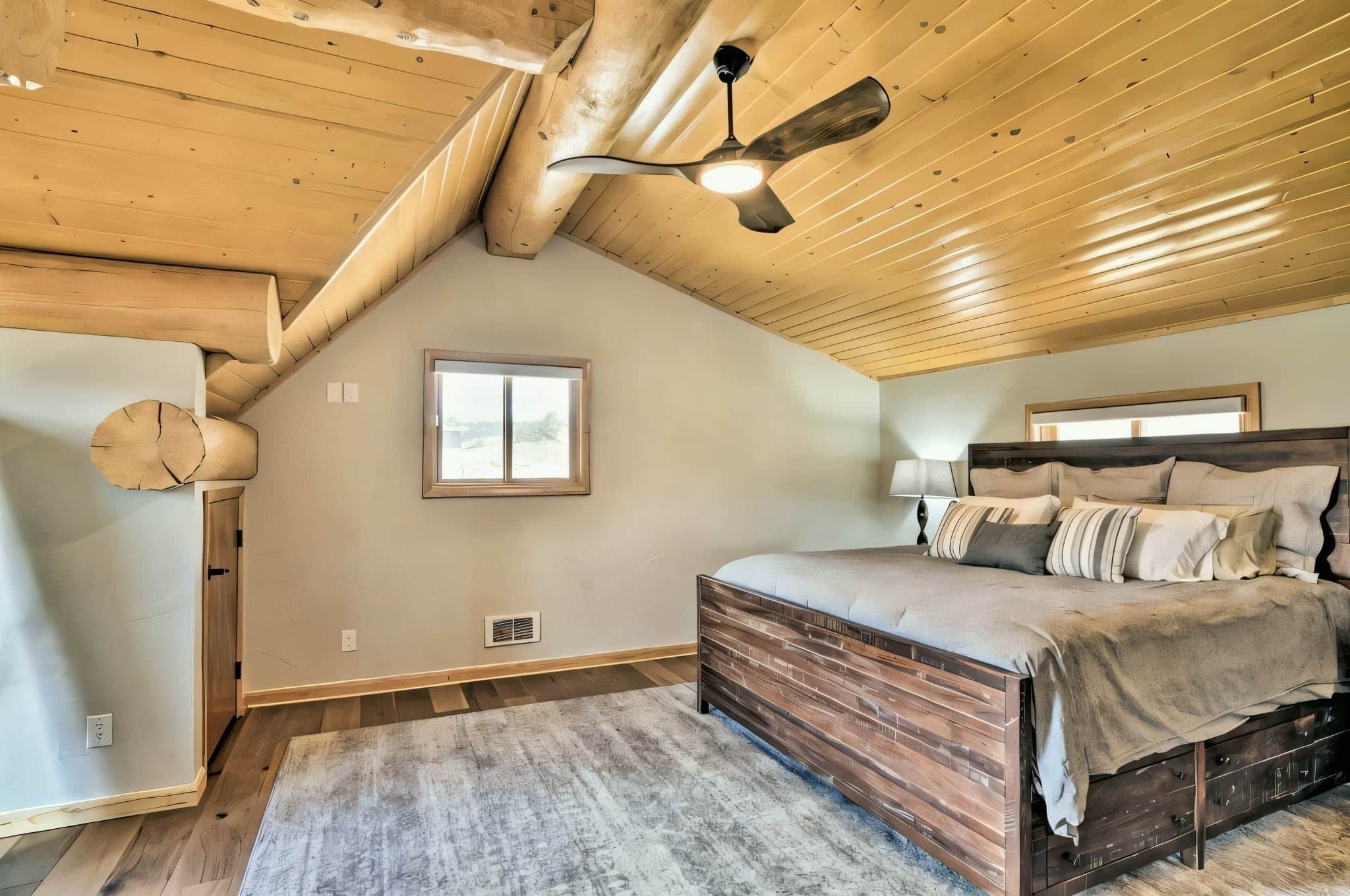 Una camera da letto con soffitto spiovente, un letto con testiera in legno, una ventola a soffitto e una finestra.