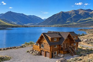 Een chalet met garage, aan een meer met bergen op de achtergrond.