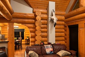 A log cabin interior with a dining area, a leather sofa, and a mounted bird.