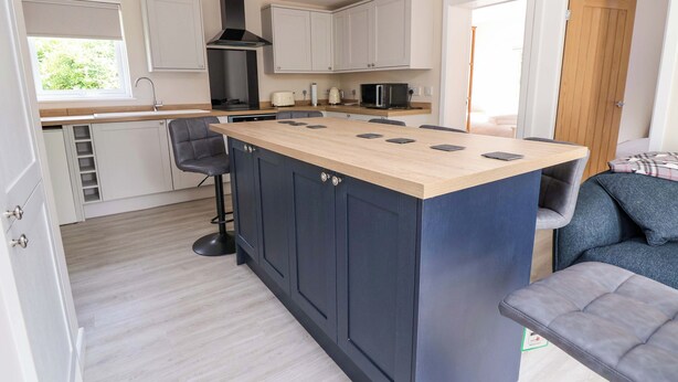 A modern kitchen with a central island, white cabinets, and a black range hood. - Cartref (Holywell)