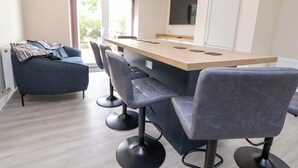 A modern kitchen with a wooden island, bar stools, and a blue sofa. - Cartref (Holywell)