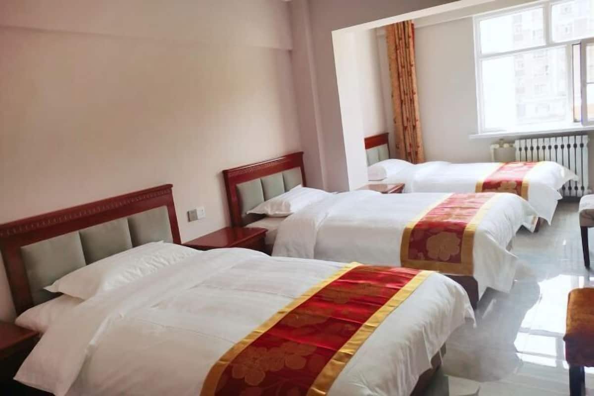 Habitación de hotel con tres camas, cada una con cabecero de madera y ropa de cama blanca.