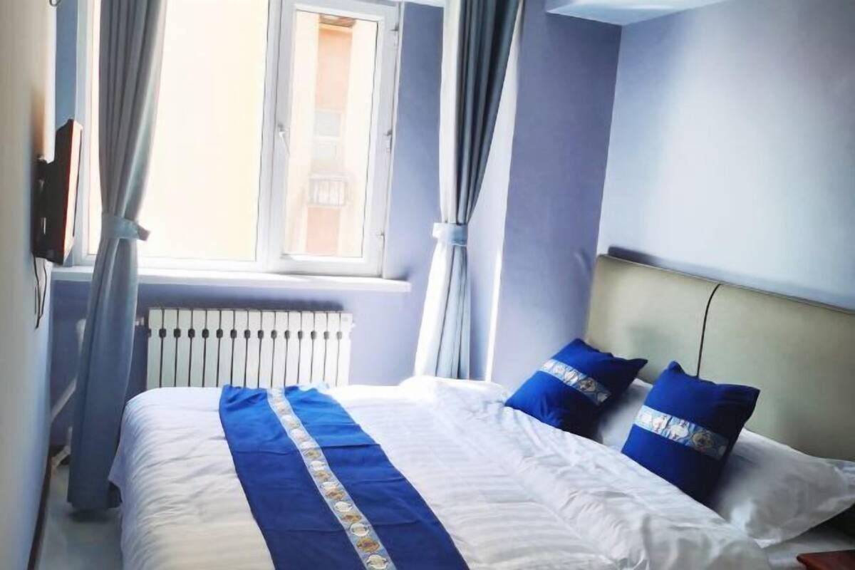 Una habitación de hotel con cama, cortinas, un radiador y una ventana.