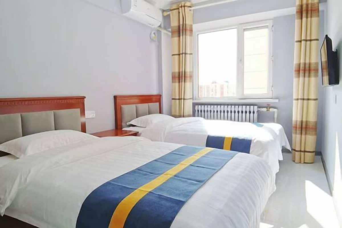 Habitación de hotel con dos camas, una ventana con cortinas, un radiador y un televisor montado en la pared.