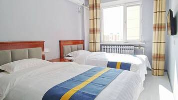 A hotel room with two beds, a window with curtains, a radiator, and a TV mounted on the wall.
