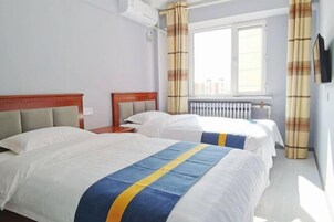 Habitación de hotel con dos camas, una ventana con cortinas, un radiador y un televisor montado en la pared.