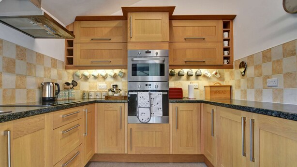 A kitchen with wooden cabinets, a double oven, and a countertop with various kitchen items. - Cottage in Hawes Near Yorkshire Dales Trails (Hawes)