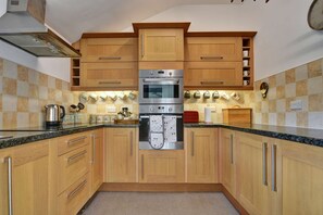 A kitchen with wooden cabinets, a double oven, and a countertop with various kitchen items. - Cottage in Hawes Near Yorkshire Dales Trails (Hawes)