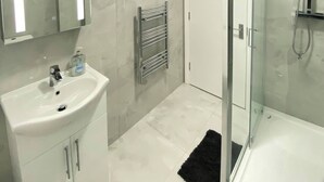 A modern bathroom with a glass shower enclosure, a white sink with a mirror, and a towel rack. - Charming 2-bedroom Apartment in the Heart of Beckenham (Beckenham)