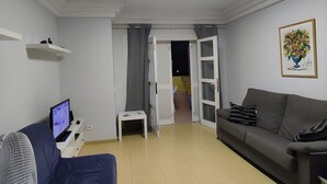A living room with a grey sofa, a small table with a TV, a fan, and a door leading to another room. - ORLANDO COSTA ADEJE (Costa Adeje)