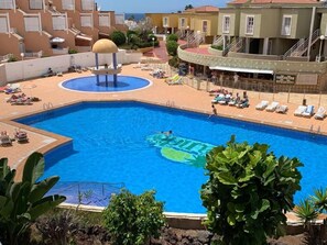 En swimmingpool med en vandinstallation i form af en sol, omgivet af liggestole og en poolbar.